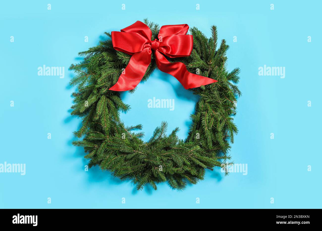 Christmas wreath made of fir branches with red bow on light blue ...