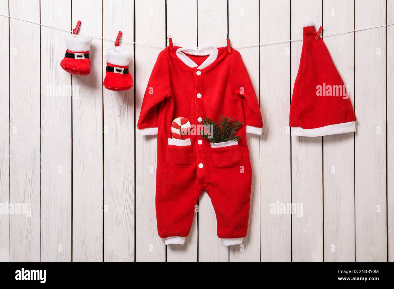 Cute Christmas baby clothes hanging on white wooden wall Stock Photo