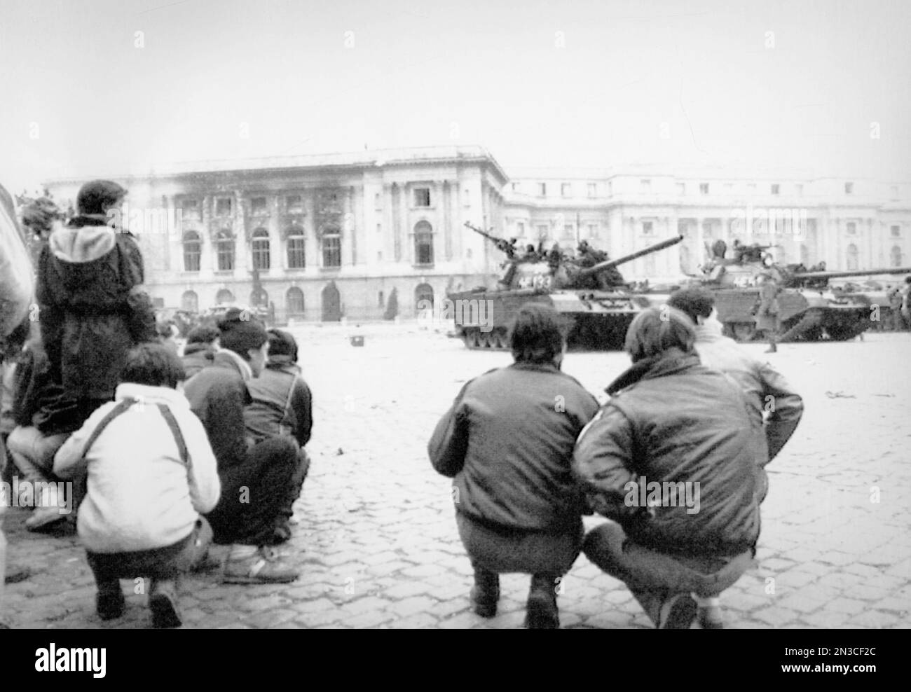 Civilians stay low and watch the tanks that are parked outside the ...