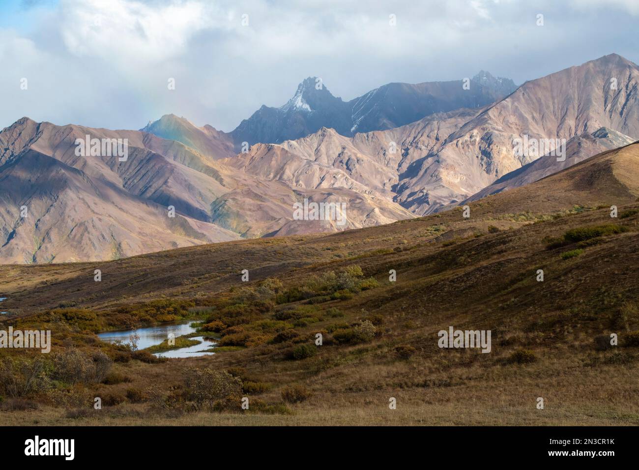 Brilliant rainbow and a cloudy sky with rugged mountain peaks near Sable Pass Stock Photo