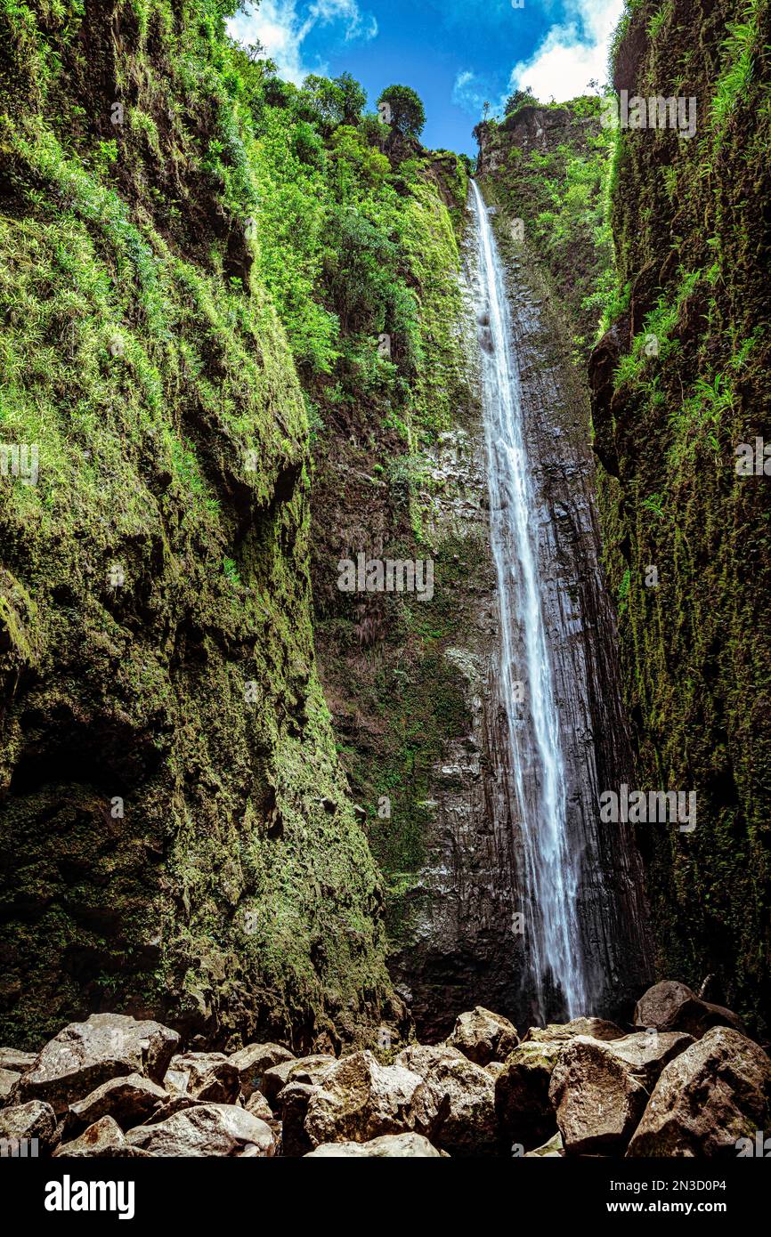 Waterfall over a steep rock cliff covered with green foliage at Hana ...