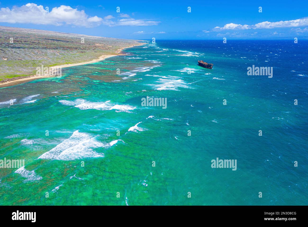 Aerial view of kiteboarders riding the waves off the coast of Shipwreck Beach in Lanai with a naval boat shipwrecked on the reef creating a dramati... Stock Photo