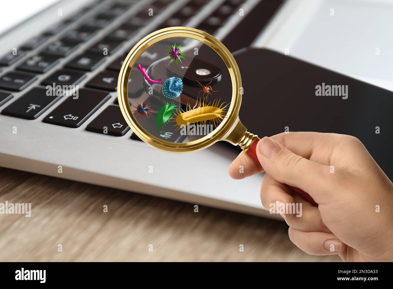 Woman with magnifying glass detecting microbes on laptop keyboard, closeup Stock Photo