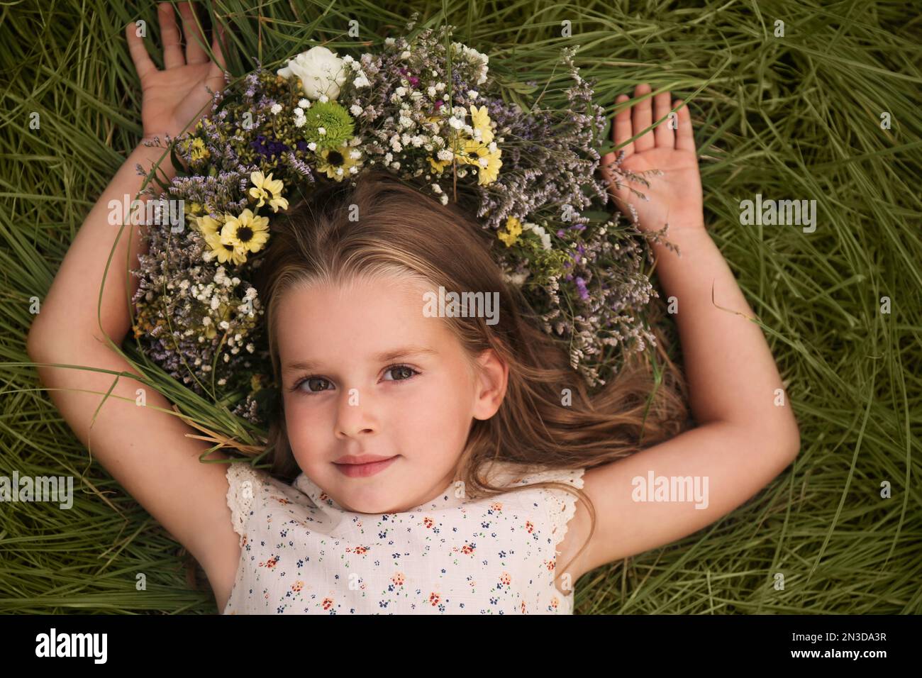 Cute little girl wearing wreath made of beautiful flowers on green ...