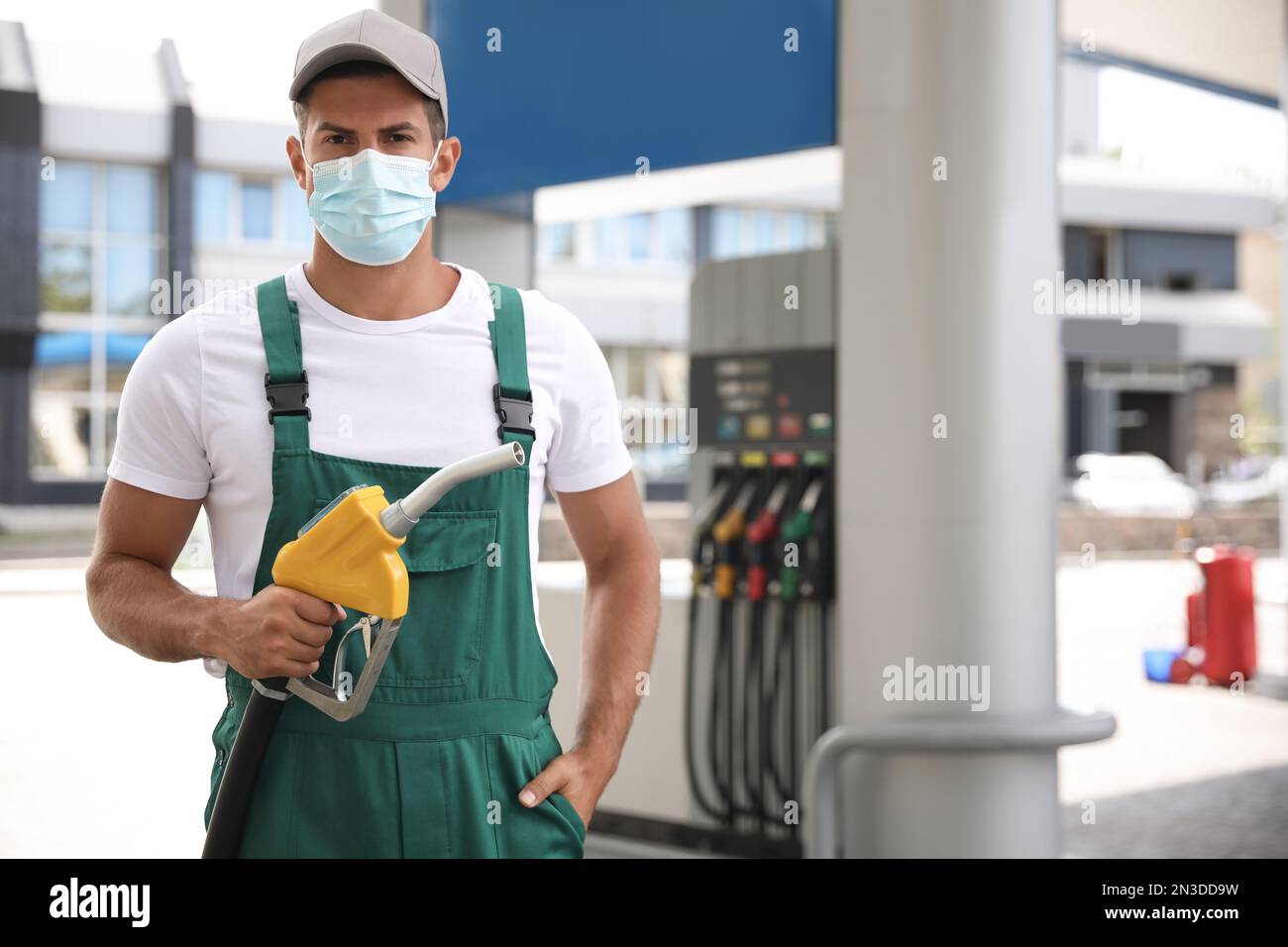Worker in mask with fuel pump nozzle at modern gas station Stock Photo