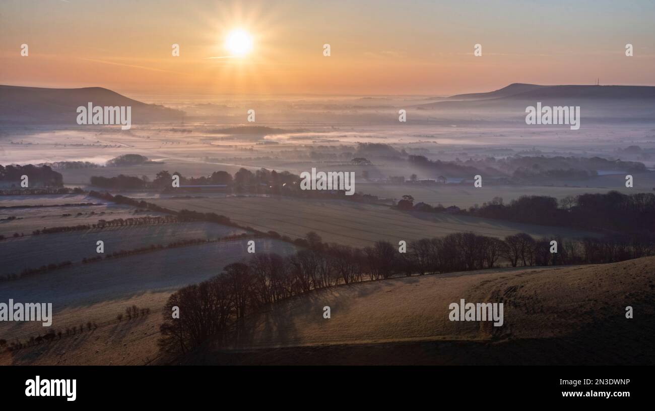 The sunrise casts long shadows over a morning mist inversion lying over the English countryside in South Downs National Park Stock Photo