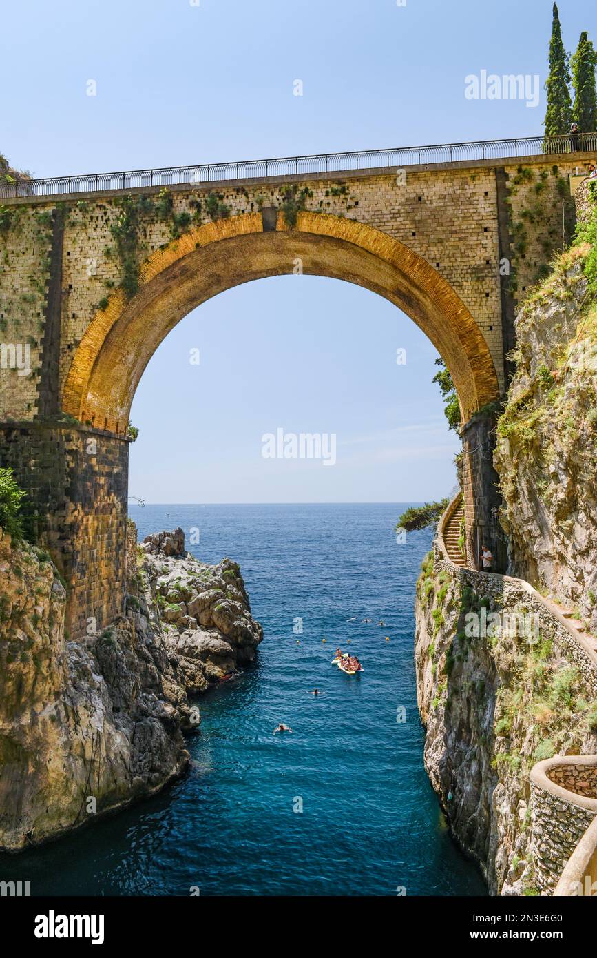People swimming and boating under an old road bridge across the bay in Furore; Furore, Salerno, Italy Stock Photo
