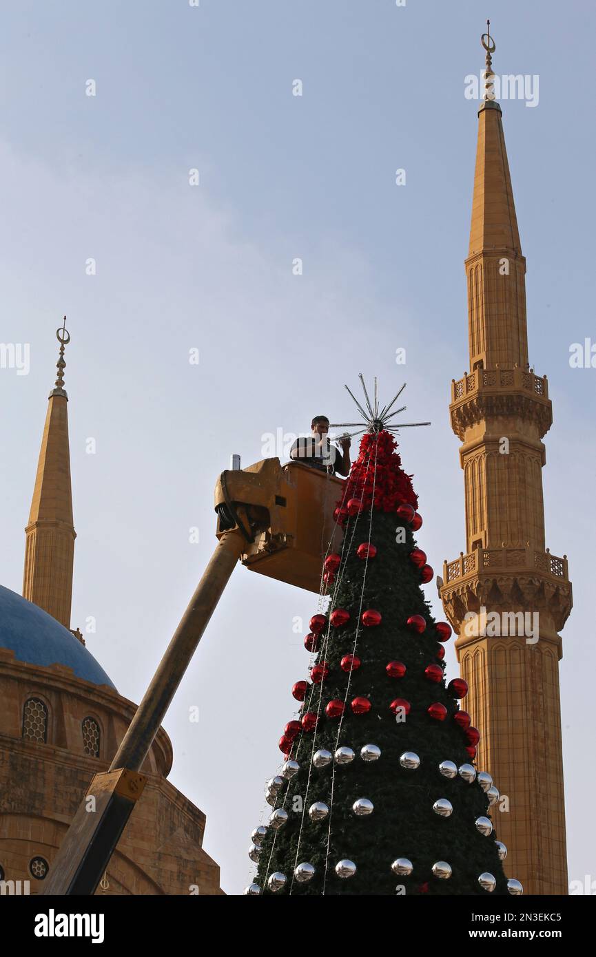 A Lebanese worker hoisted aloft by a crane decorates a Christmas tree in front of the Muhammad