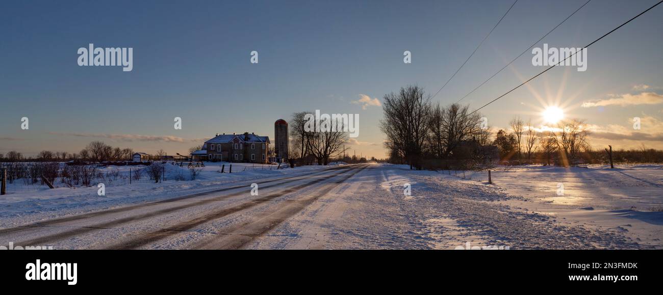 Countryside on a winter evening with the glowing sun setting over the snow-covered fields; Ottawa Valley, Ontario, Canada Stock Photo