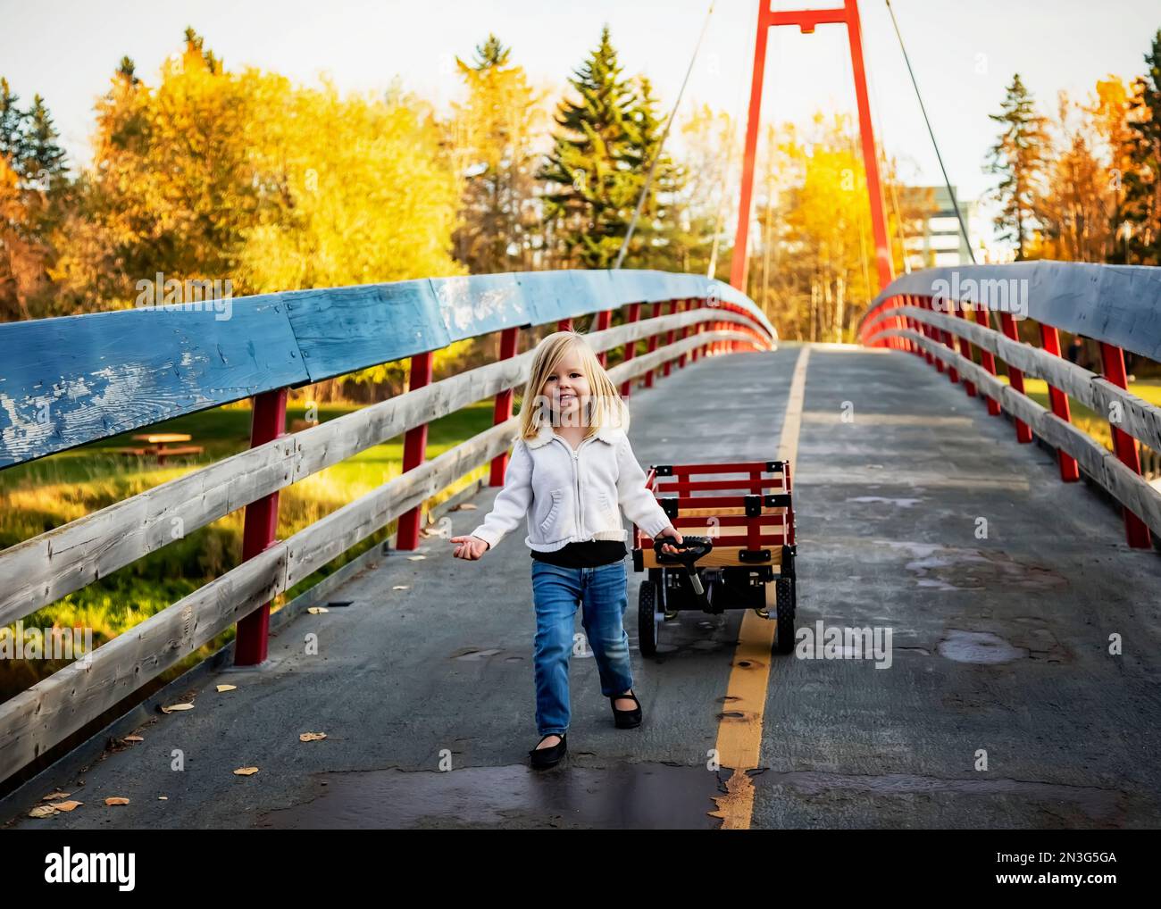 Young girl pulling her wagon across a bridge over a river in a city