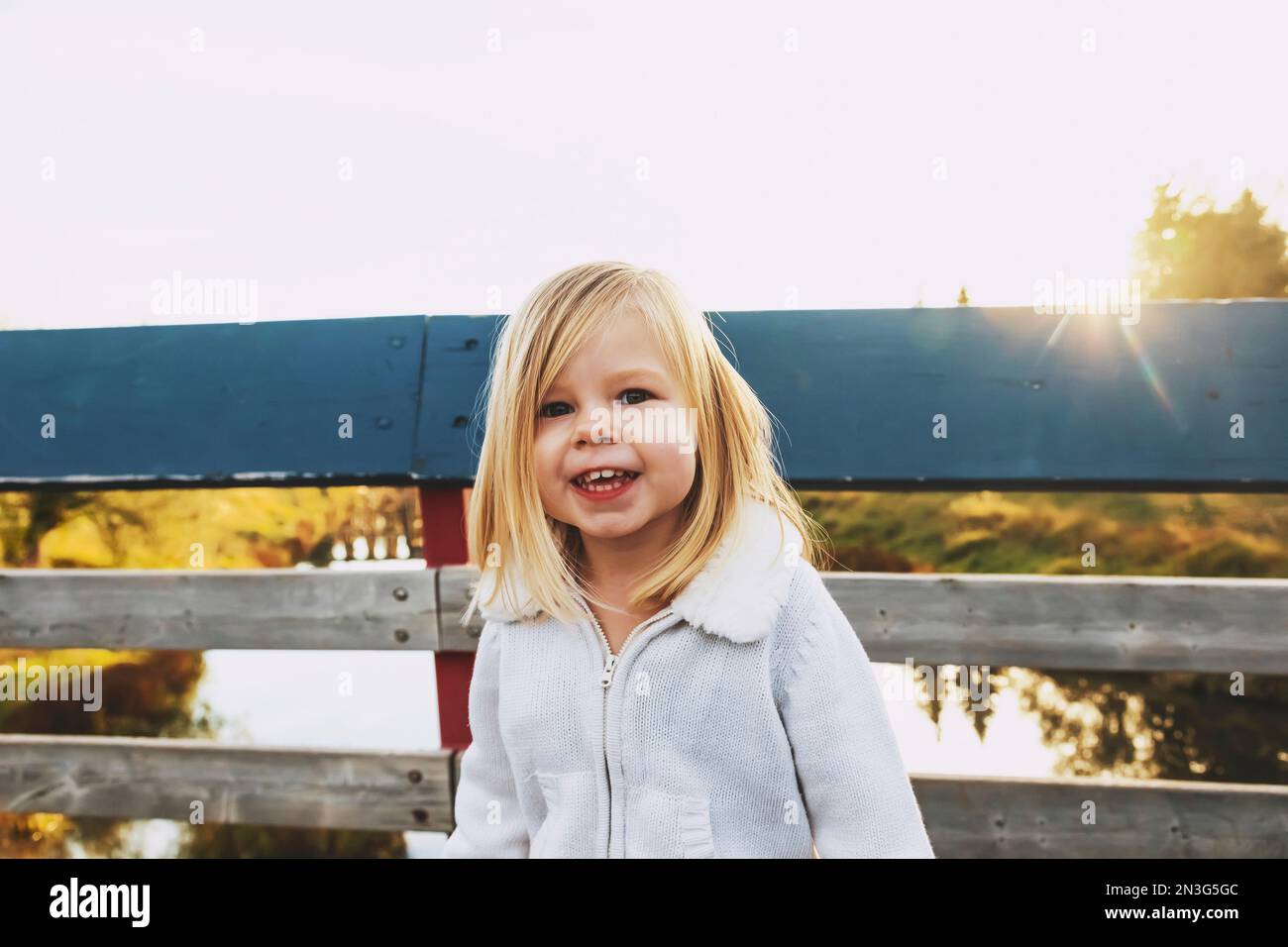 Young girl posing for a portrait while standing on a bridge over a river in a city park during the fall season; St. Albert, Alberta, Canada Stock Photo