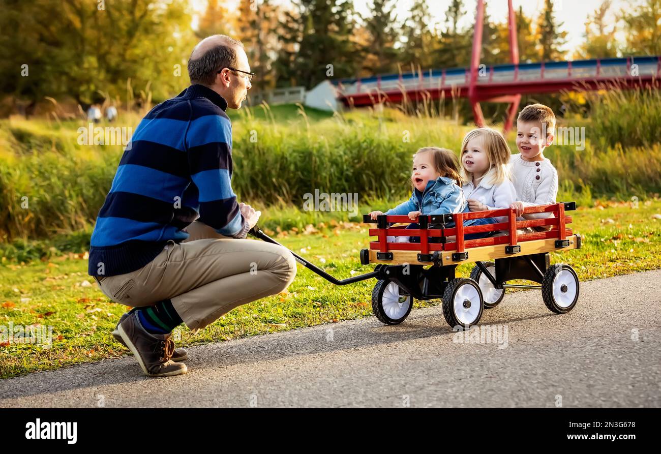 A father pulling his young children in a wagon along a river in a city ...