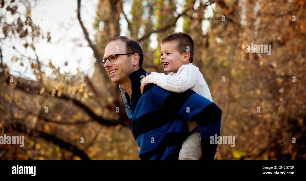 A father playing with his young son who is piggy back riding during a family outing at a city park during the fall season; St. Albert, Alberta, Canada Stock Photo