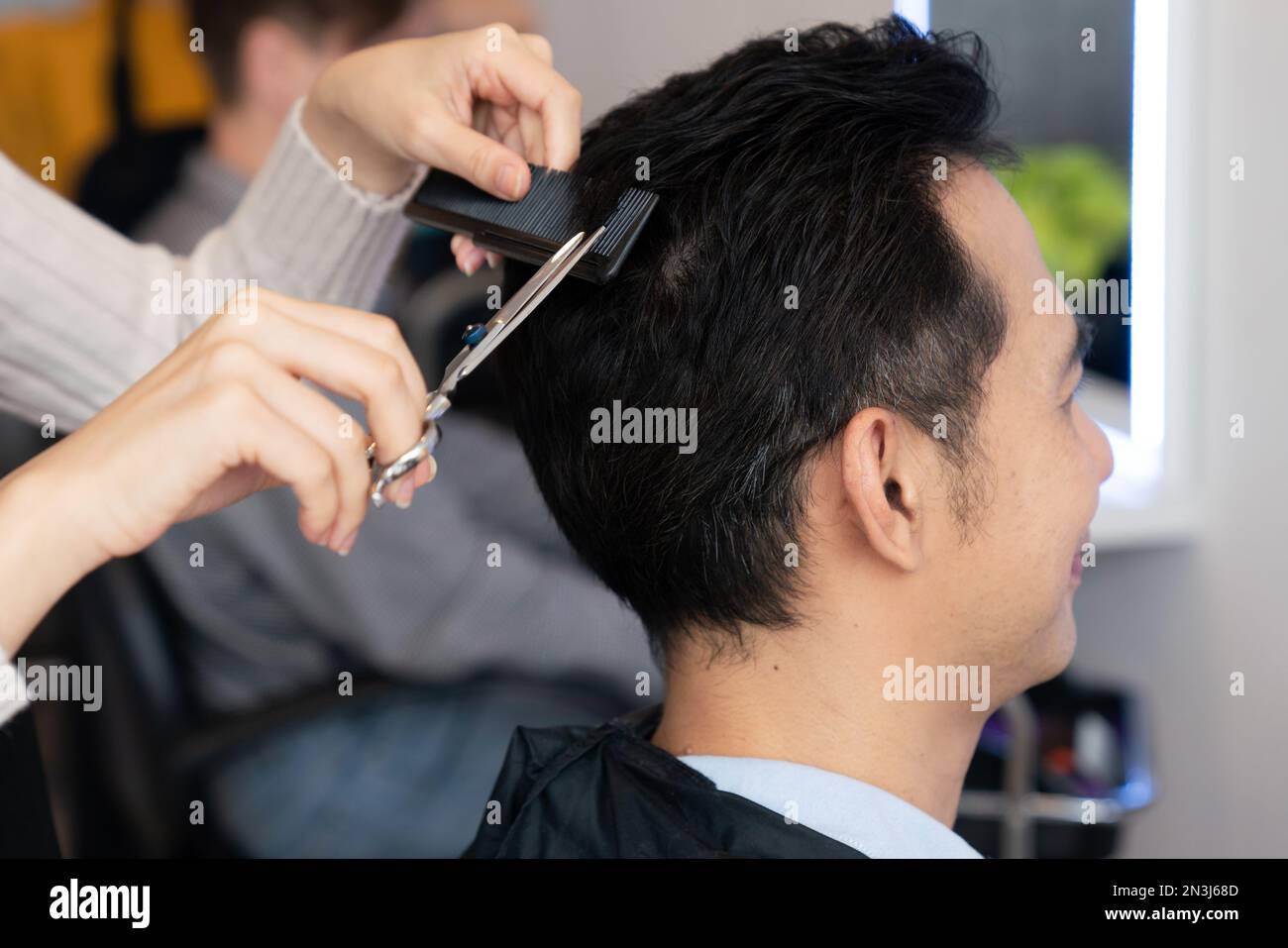 Closeup asian female barber making haircut for male customer with male hairstyle in qualified