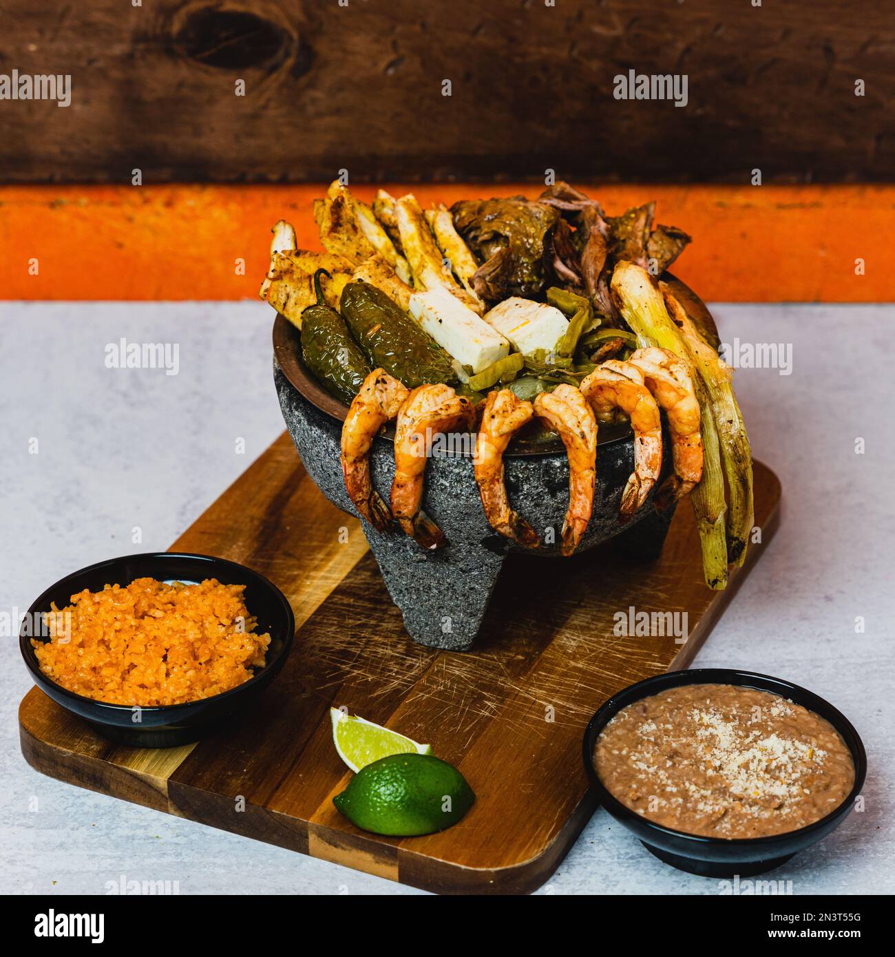 A closeup of a mixed meats in molcajete next to rice and beans on a wooden board Stock Photo