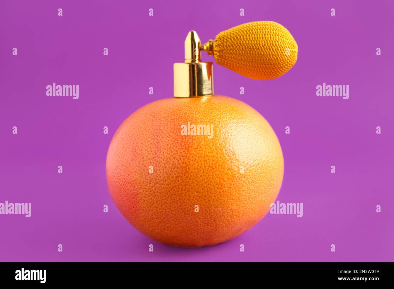 Grapefruit with vintage atomizer imitating perfume on violet background Stock Photo