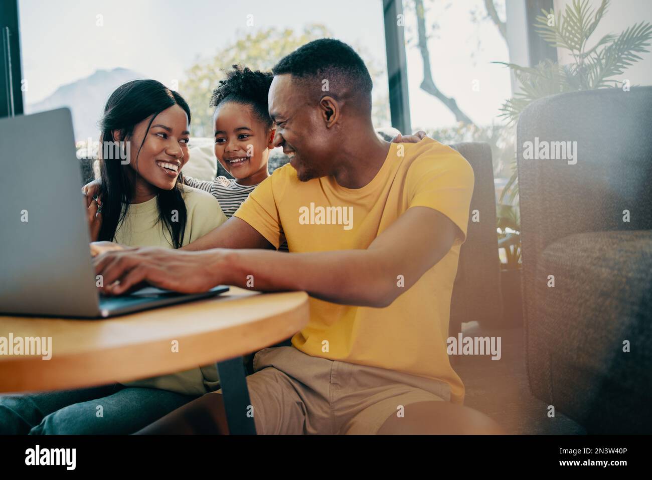 Black family using a laptop together in the living room, parents browsing online entertainment with their little child. Modern couple parenting a pres Stock Photo
