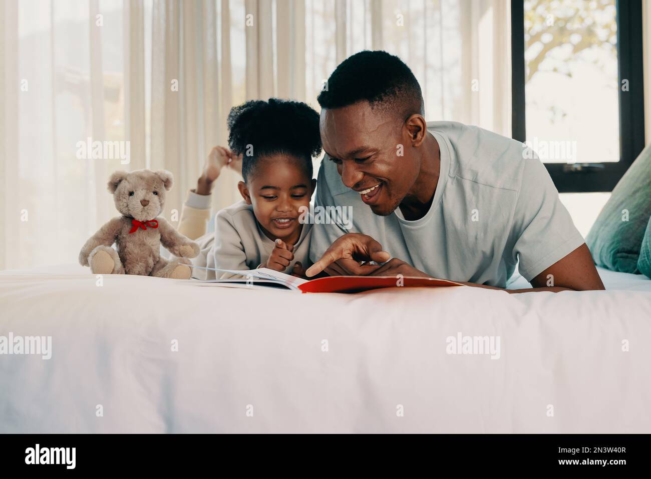 Daddy reads a story with his daughter on the weekend. Father and daughter lying on a bed with a story book. Parent spending quality time with his kid Stock Photo