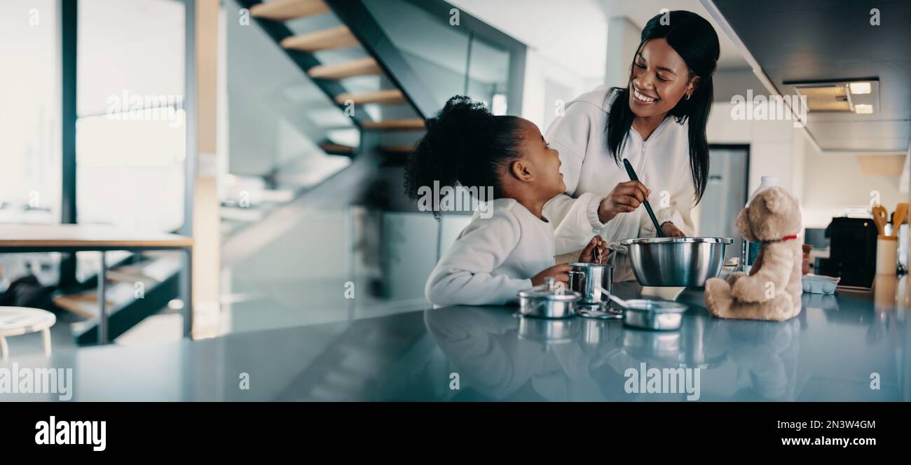 Mother and daughter spending time in the kitchen cooking together. Little child learning how to make food from her mom. Happy family spending quality Stock Photo