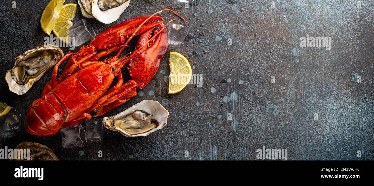 Boiled cooked red whole lobster ready to eat and fresh open oysters served with lemon wedges and ice cubes top view flat lay on blue concrete stone Stock Photo