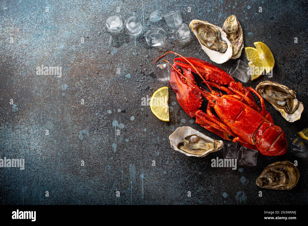 Boiled cooked red whole lobster ready to eat and fresh open oysters served with lemon wedges and ice cubes top view flat lay on blue concrete stone Stock Photo