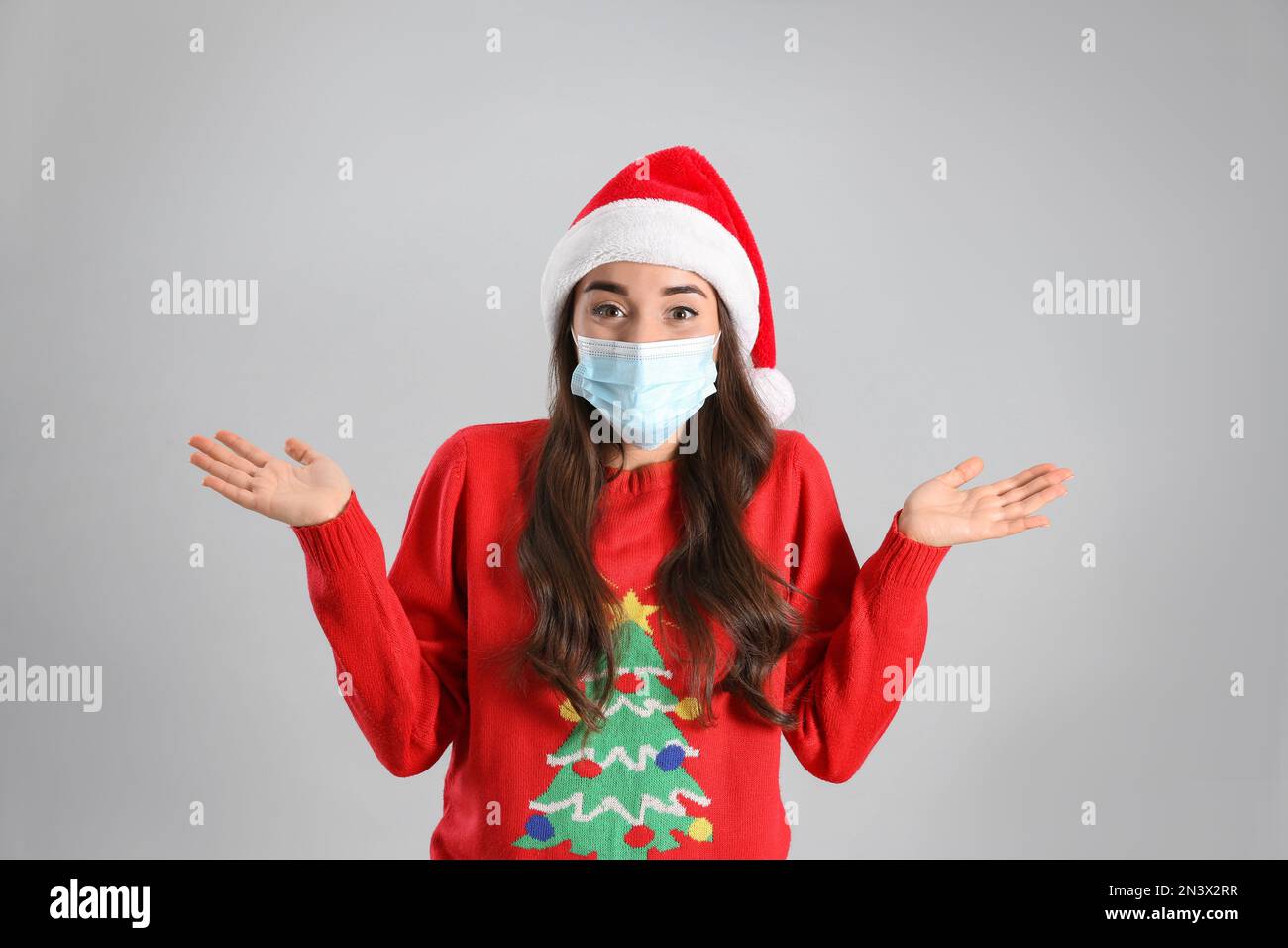 Beautiful emotional woman wearing Santa Claus hat and medical mask on ...