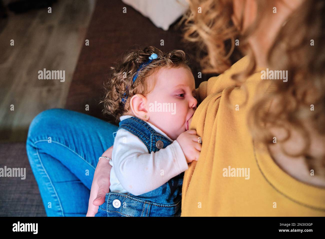 Close-up of a woman breastfeeding daughter sitting on the couch at home. Stock Photo