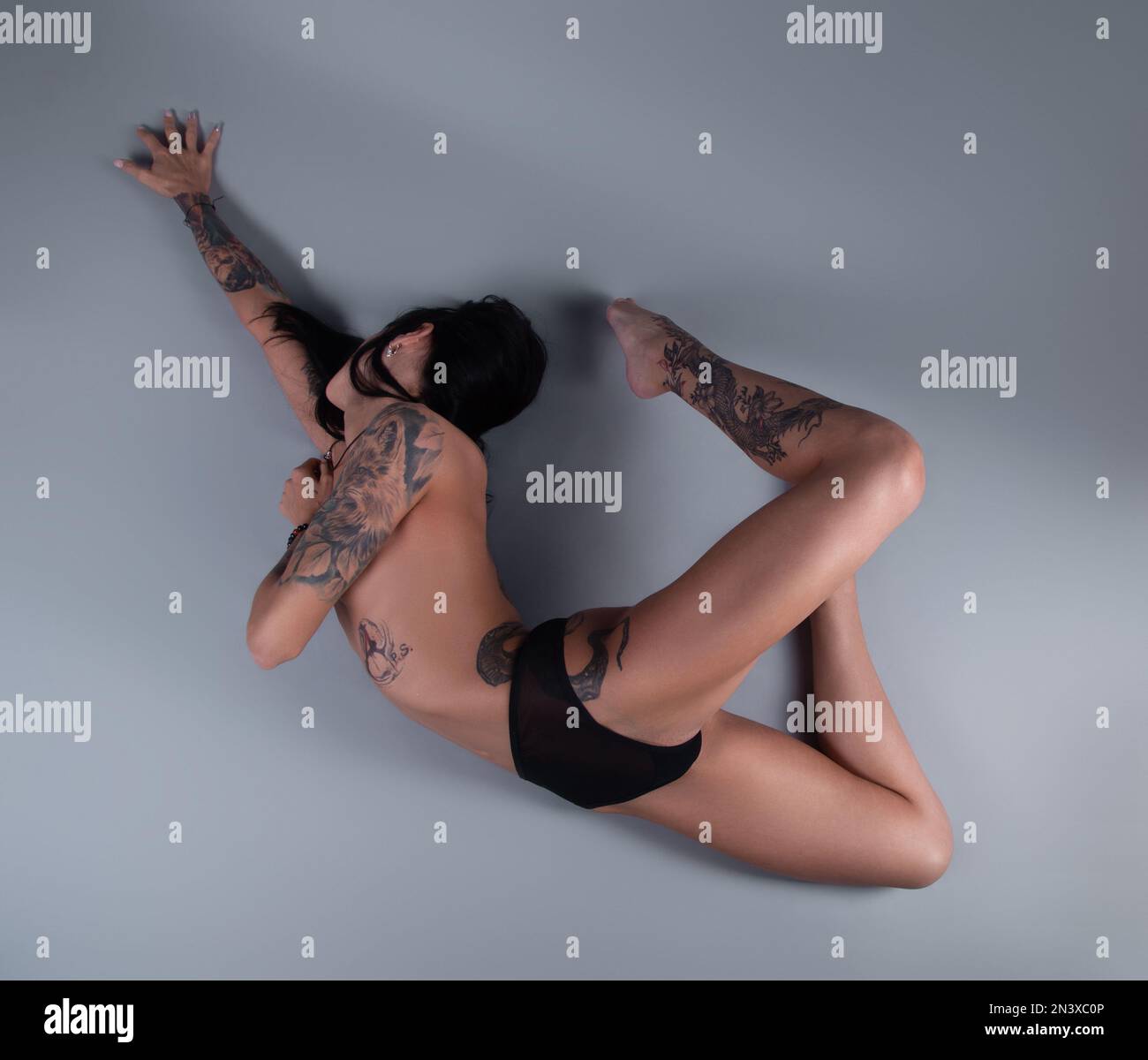 Image of stretching topless girl with tattoo in black panties on gray background Stock Photo