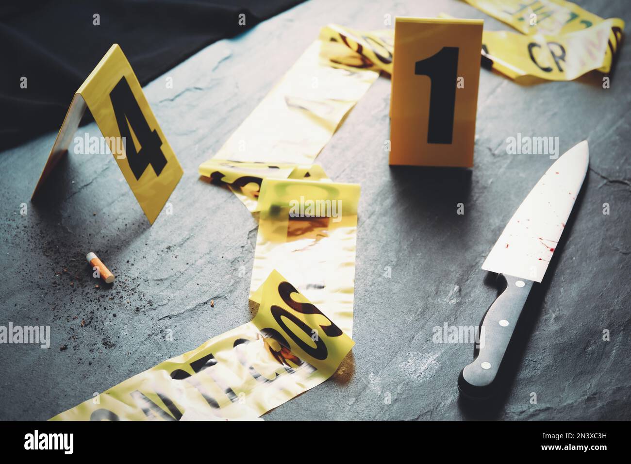 Evidence markers, yellow tape and knife on black slate table. Crime