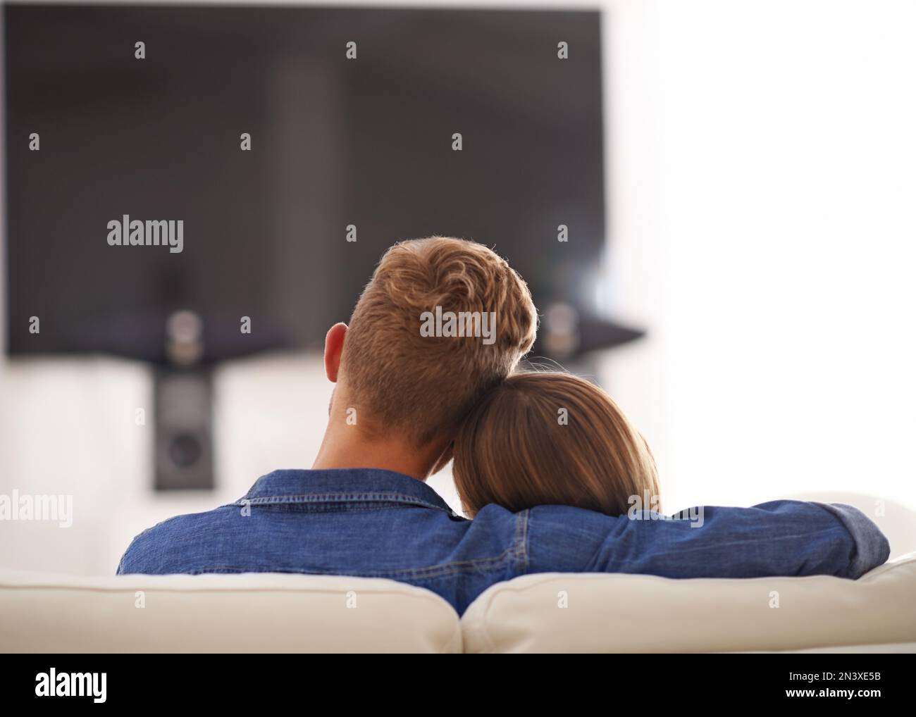 Lets cuddle on the couch all day. Young couple cuddling together in front of the TV Stock Photo
