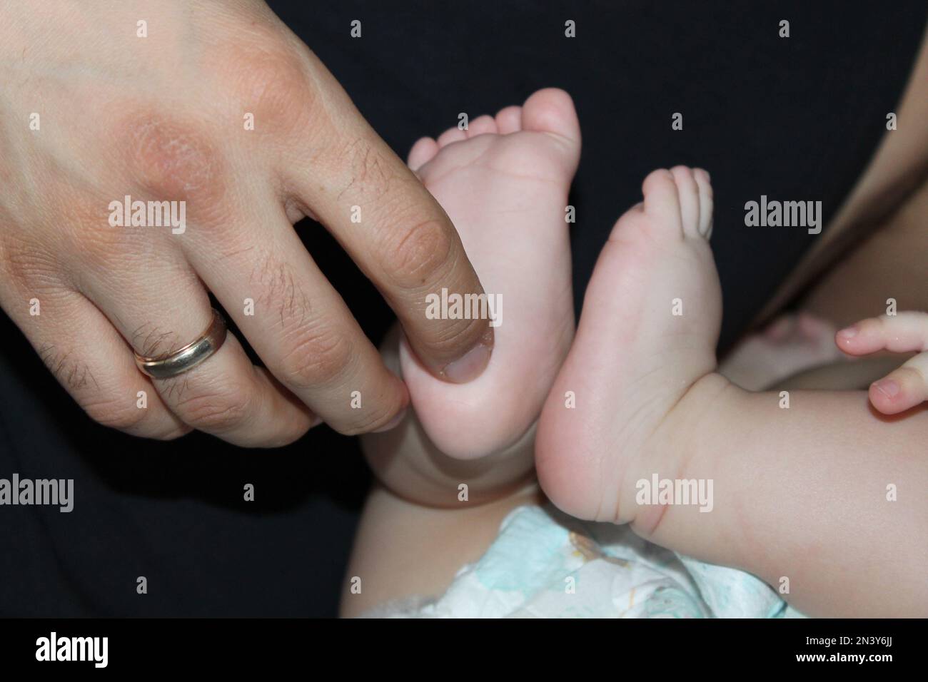 Children's feet in hands of father. Dad tickles feet of kid. Baby counts toes. Happy father Stock Photo