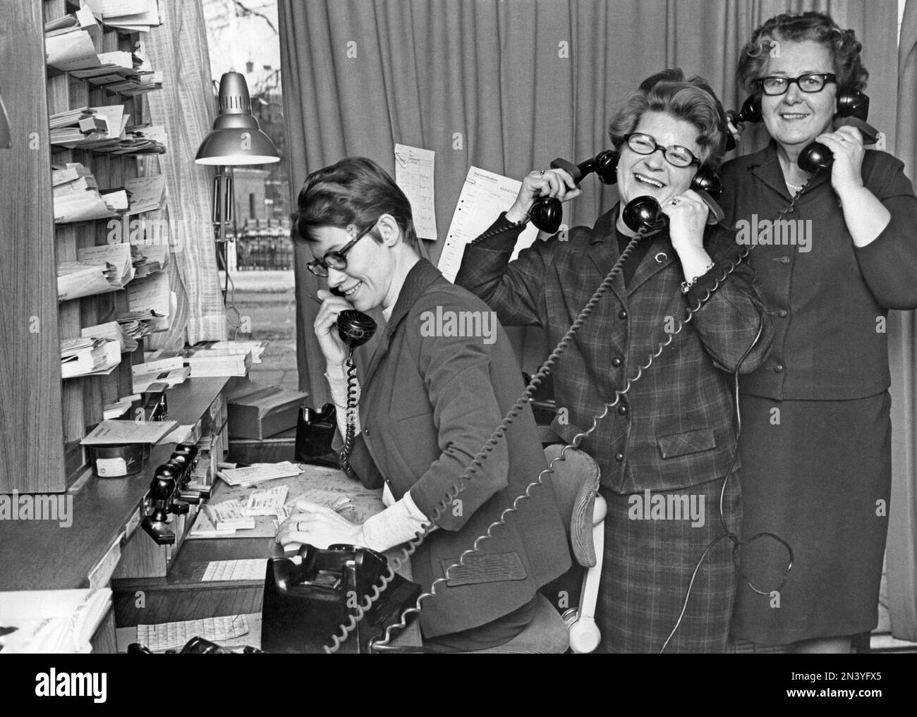 In the 1960s. Three women having fun at work, holding multiple telephones and laughing. Sweden 1967 Stock Photo