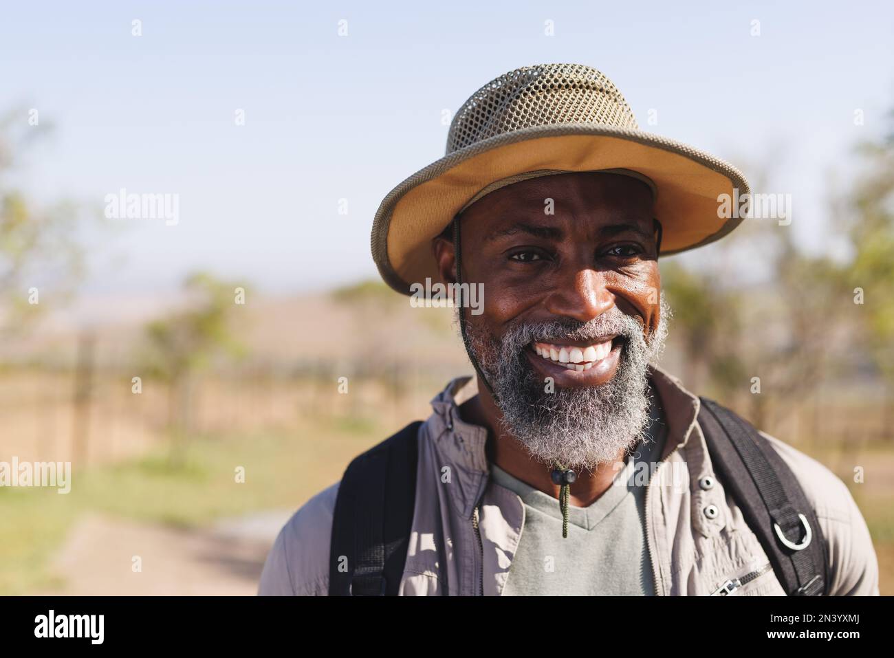 Portrait of smiling bearded african american senior man wearing hat hiking in forest under clear sky Stock Photo