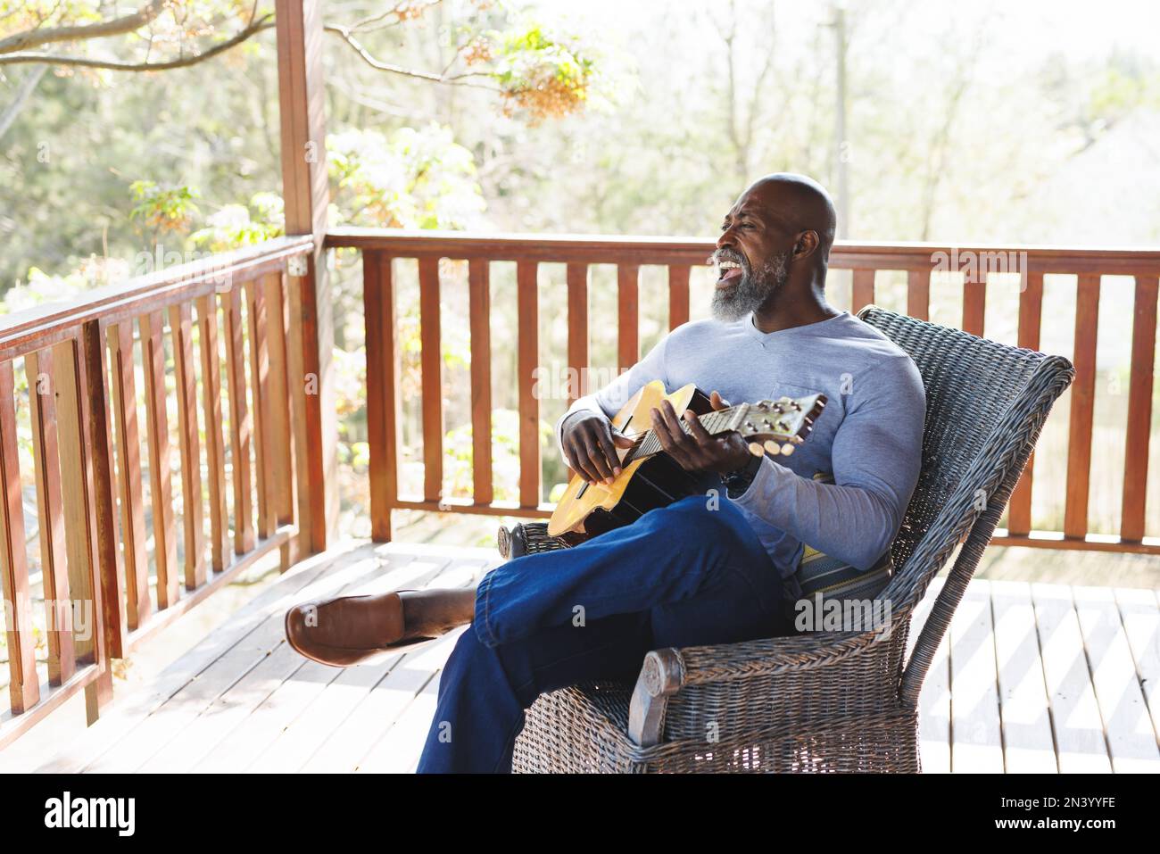 Bald african american senior man playing guitar while sitting on chair in balcony at log cabin Stock Photo