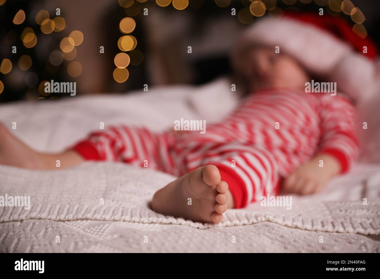 Baby in Christmas pajamas and Santa hat sleeping on bed indoors, focus