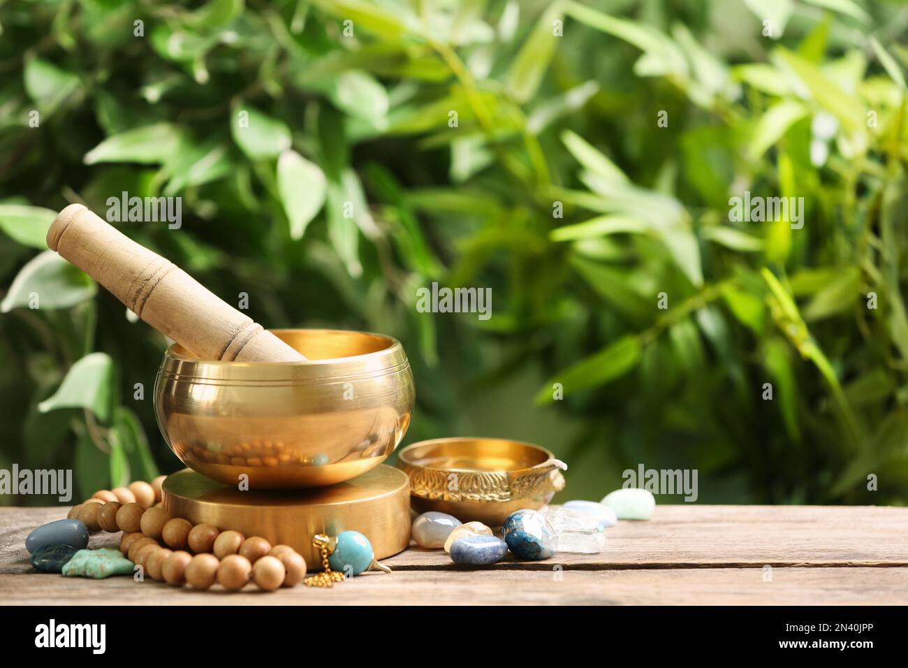 Composition with tibetan singing bowl and different gemstones on wooden table outdoors, space for text. Sound healing Stock Photo