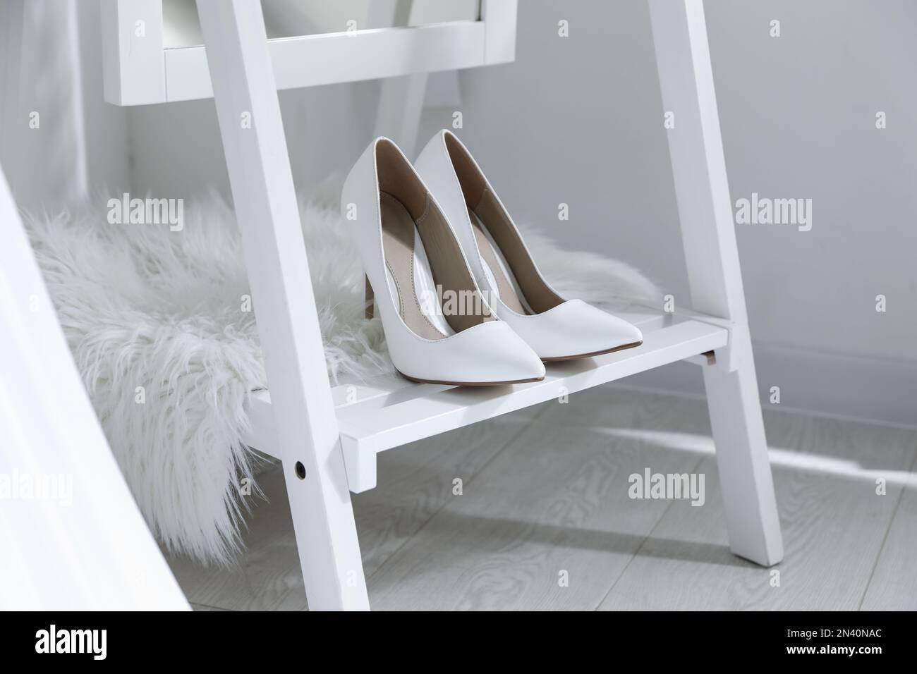 Pair of white wedding high heel shoes on wooden rack indoors Stock Photo