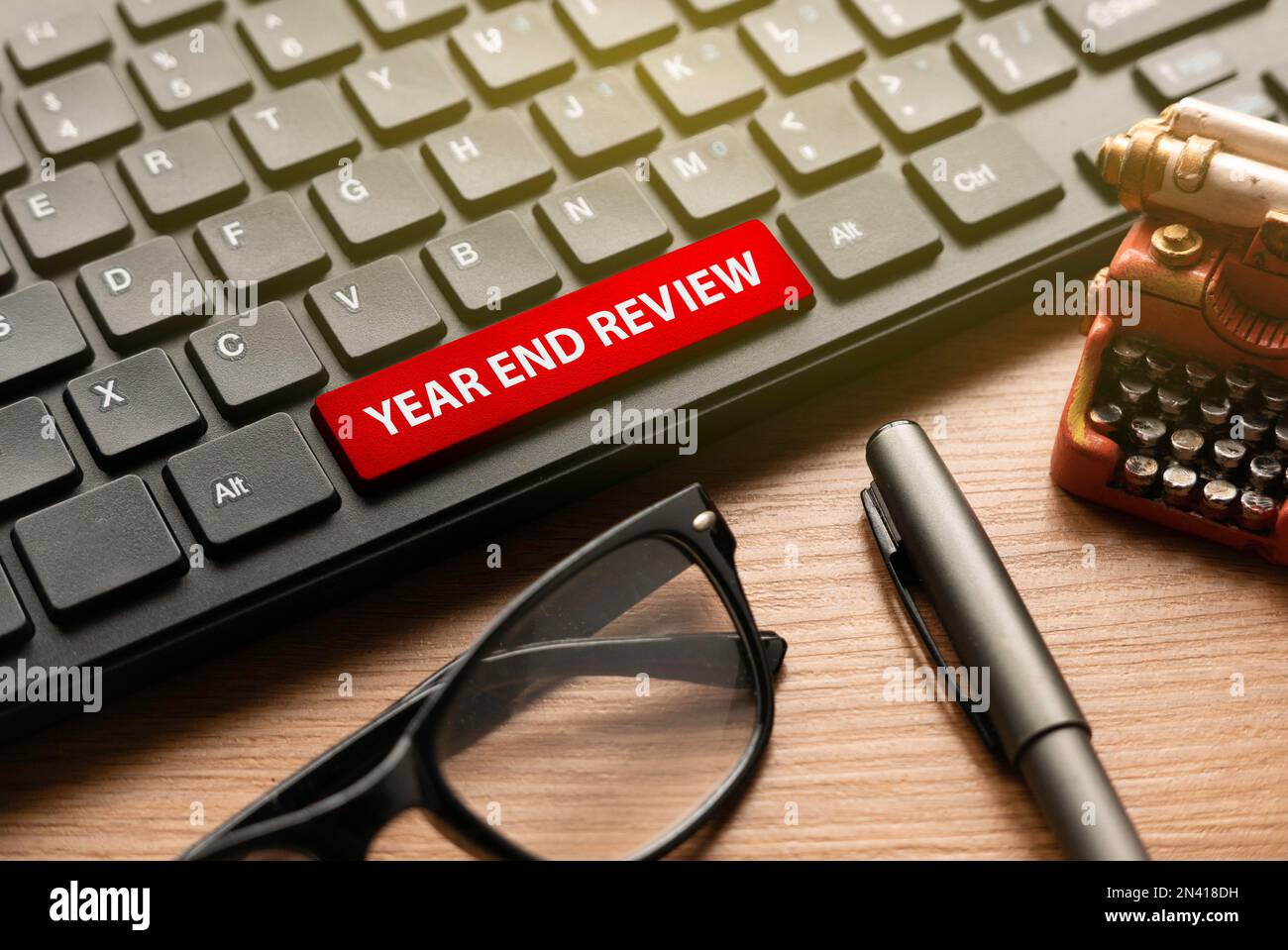 Glasses,pen, miniature typewriter and computer keyboard with red button written with Year End Review. Stock Photo
