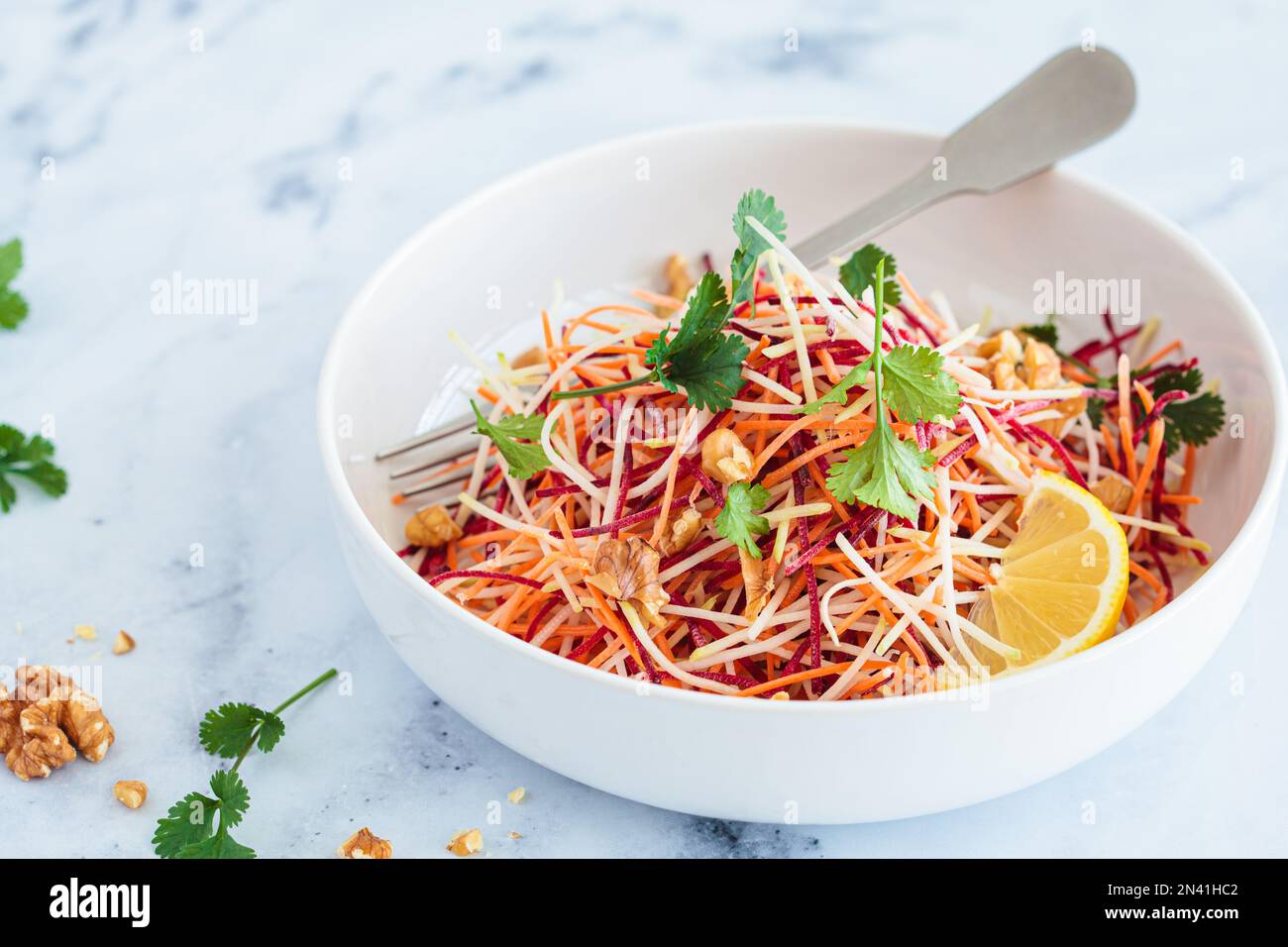 Spring carrots, beets, cabbage salad with nuts and herbs in a white bowl. Stock Photo