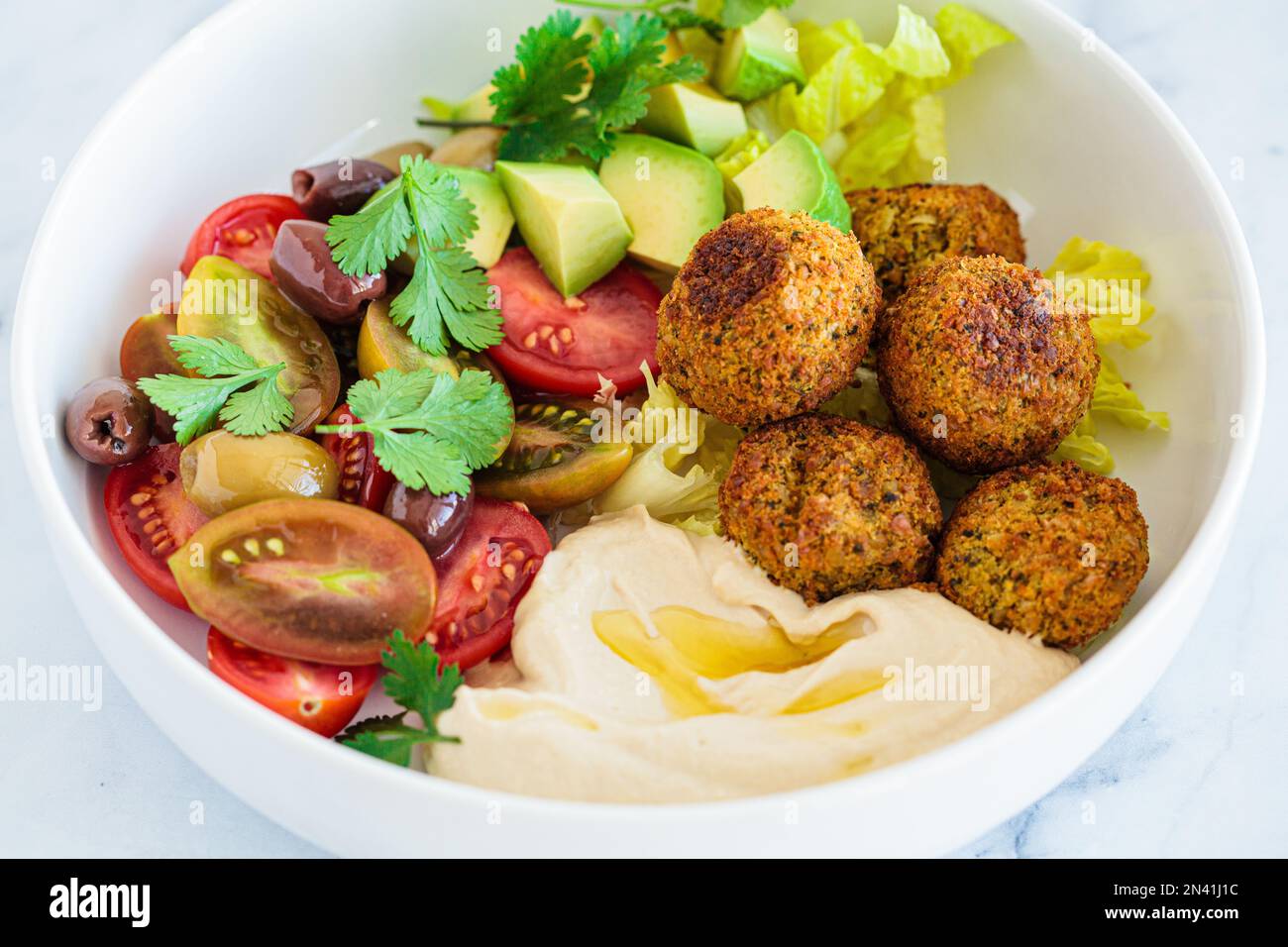Falafel salad plate with lettuce, tomatoes, avocado, hummus and olives. Healthy vegan food, Israeli cuisine. Stock Photo