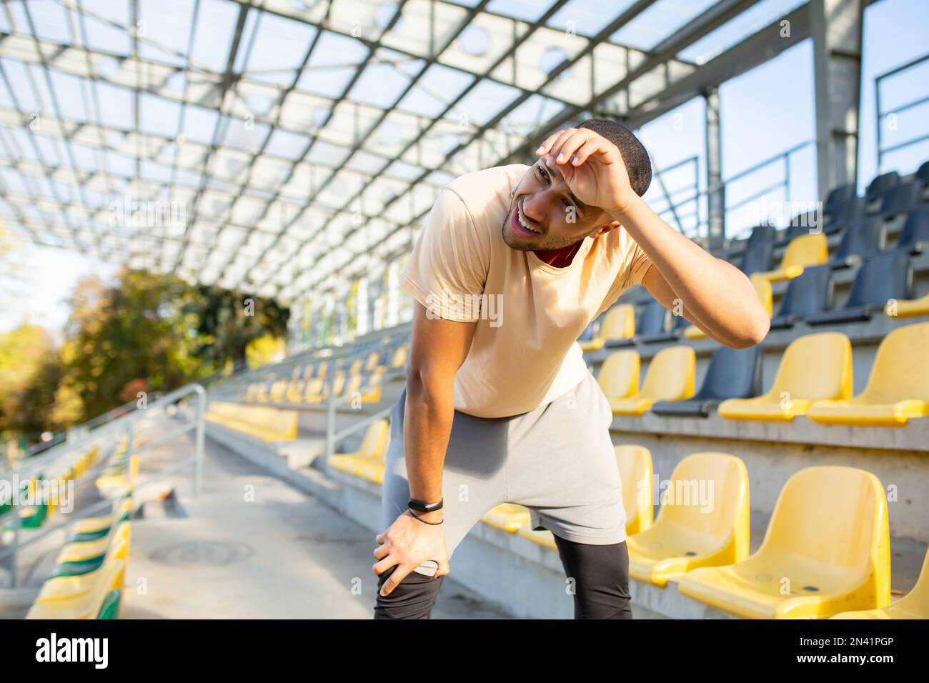 Tired hispanic athlete bent over and breathing after jogging, man doing