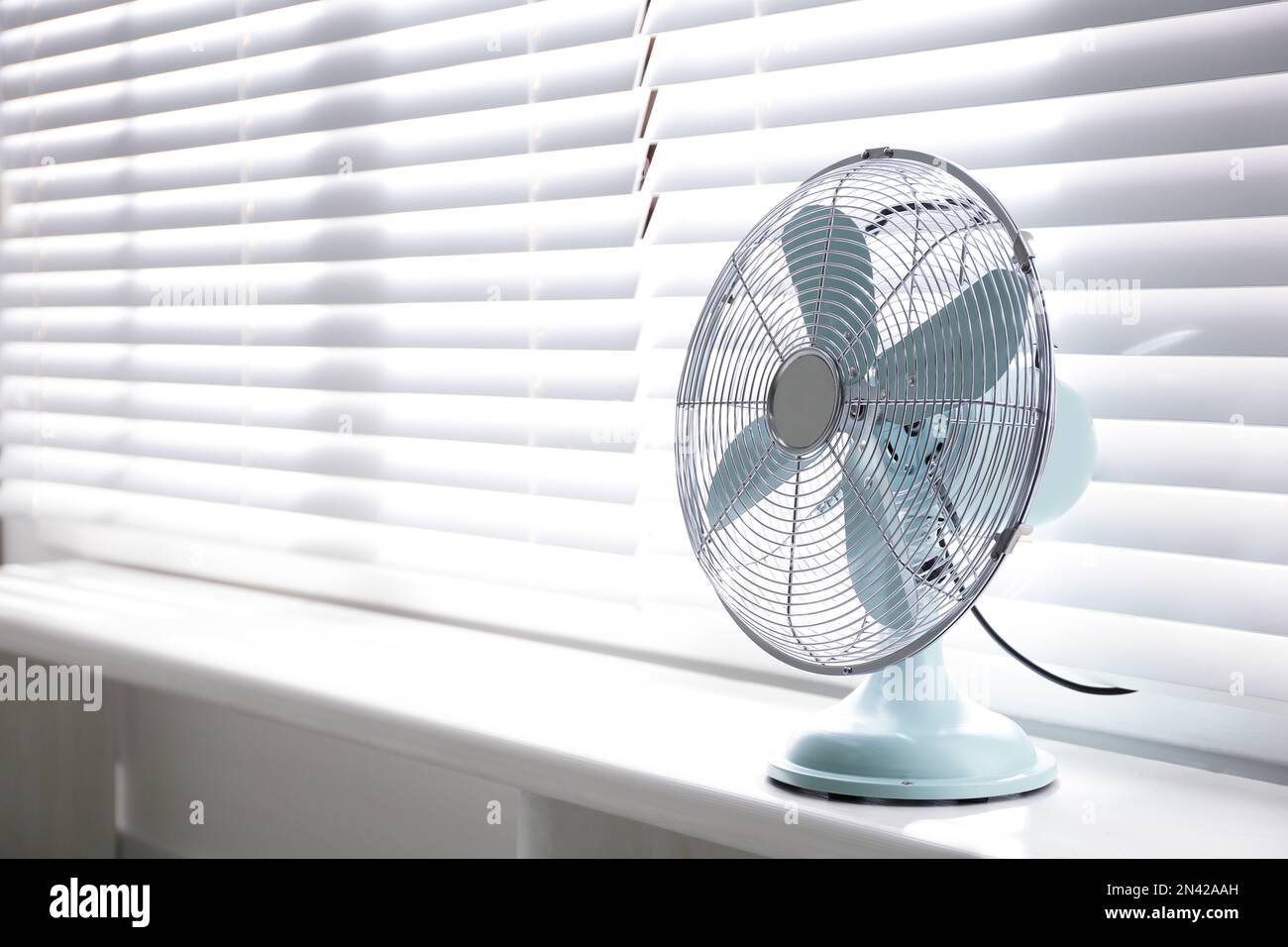 Modern electric fan on window sill indoors. Space for text Stock Photo