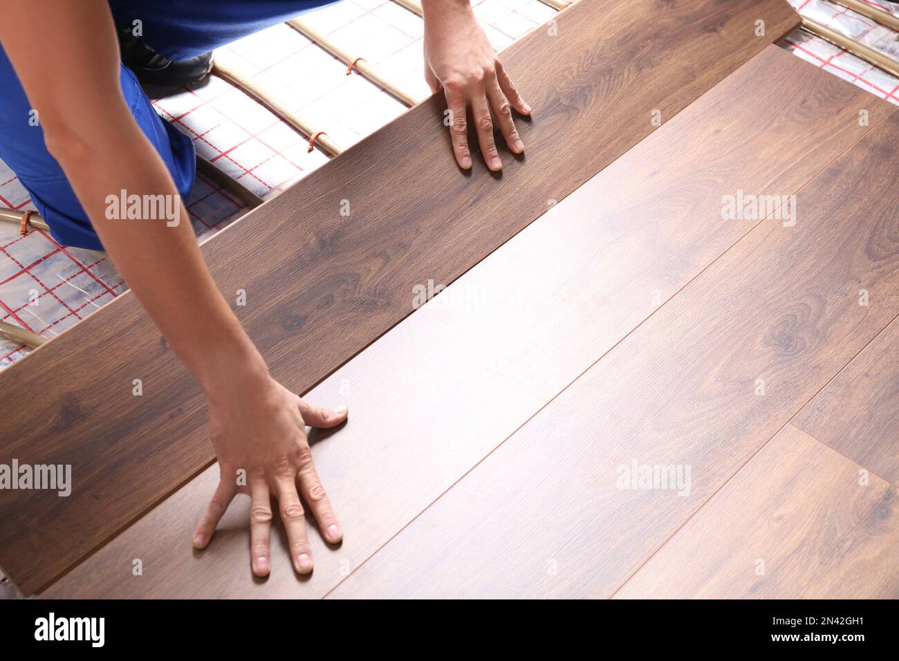 Worker installing new wooden laminate over underfloor heating system