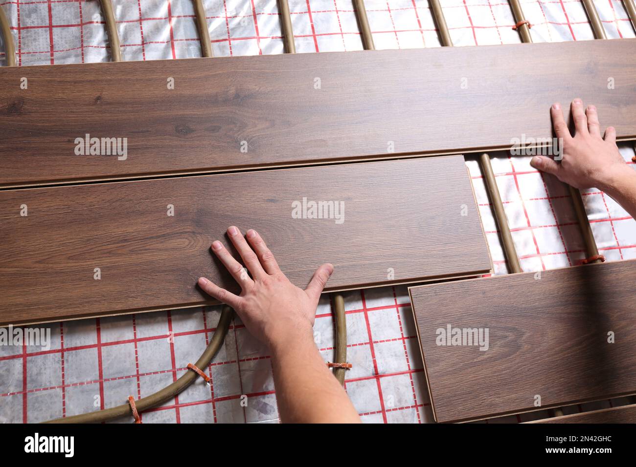 Worker installing new wooden laminate over underfloor heating system