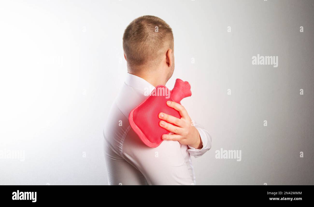 A man holds a red medical heating pad with hot water near his shoulder