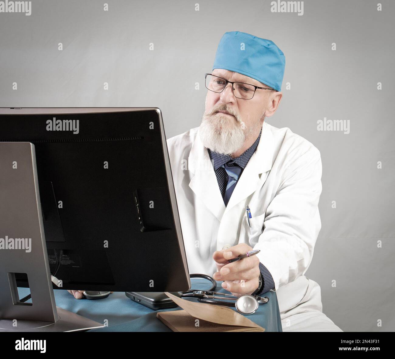 Photo of elderly doctor using prescription laptop, glasses, expert, uniform isolated on gray background. Stock Photo