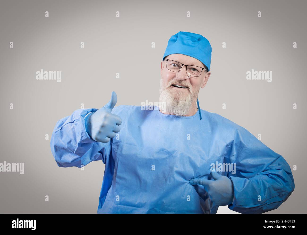 Infectious disease doctor with a gray beard in a blue protective overalls and rubber gloves shows a thumbs up. Stock Photo