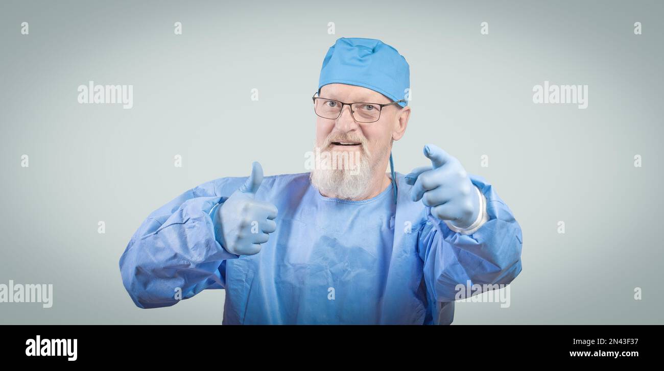 Infectious disease doctor with a gray beard in a blue protective overalls and rubber gloves shows a thumbs up. Stock Photo
