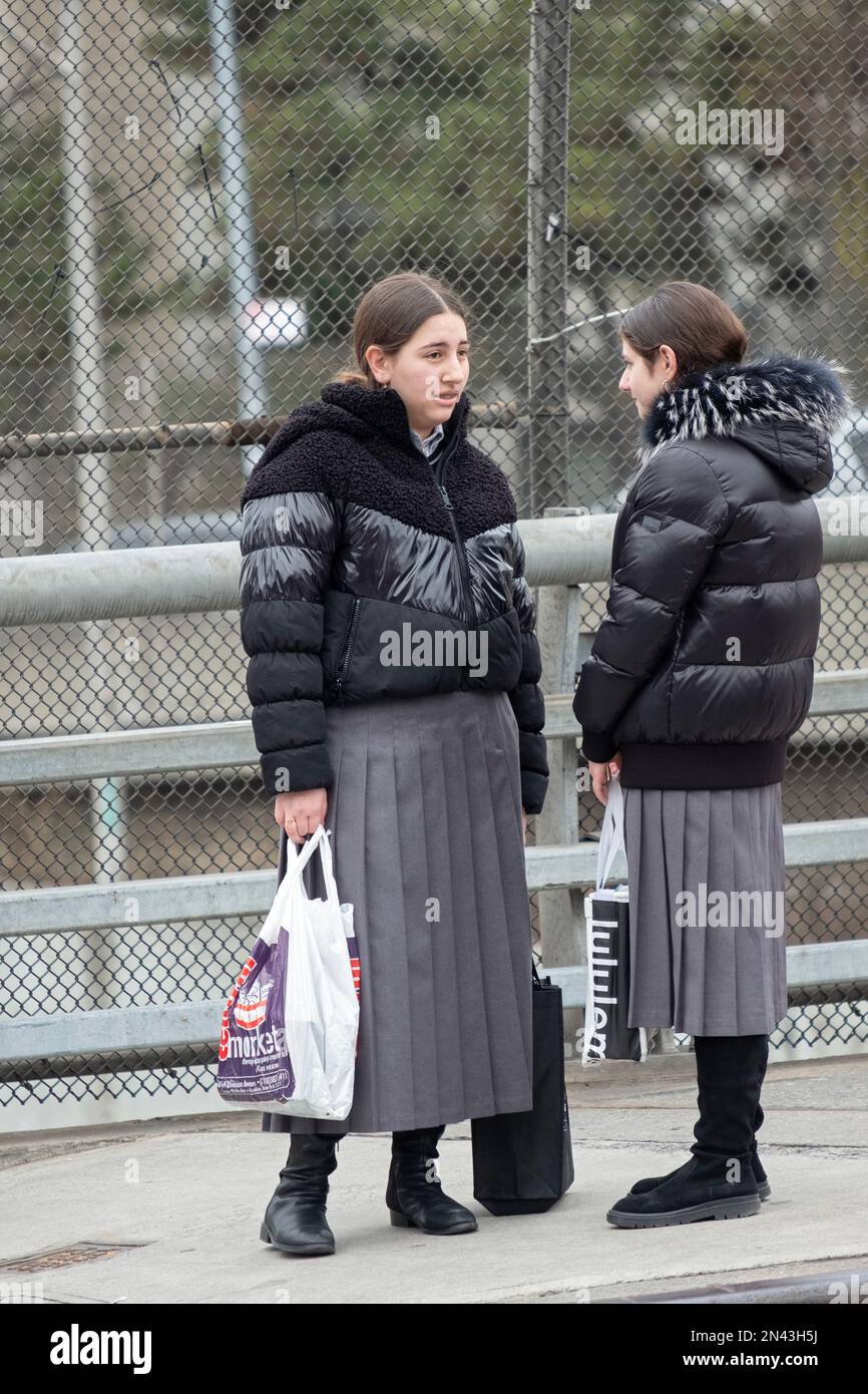 2 modestly dressed orthodox Jewish girls have a conversation. The matching pleated skirts are school uniforms.In brooklyn, New York. Stock Photo