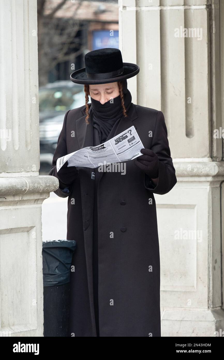On a winter day a Hasidic Jewish man reads a  flyer outside a Satmar synagogue with a scarf tied over his mouth. In Williamsburg, Brooklyn, NYC. Stock Photo